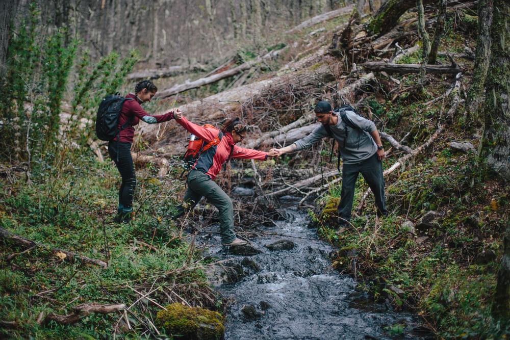 Estudiantes cruzan un arroyo en el bosque tomados de la mano