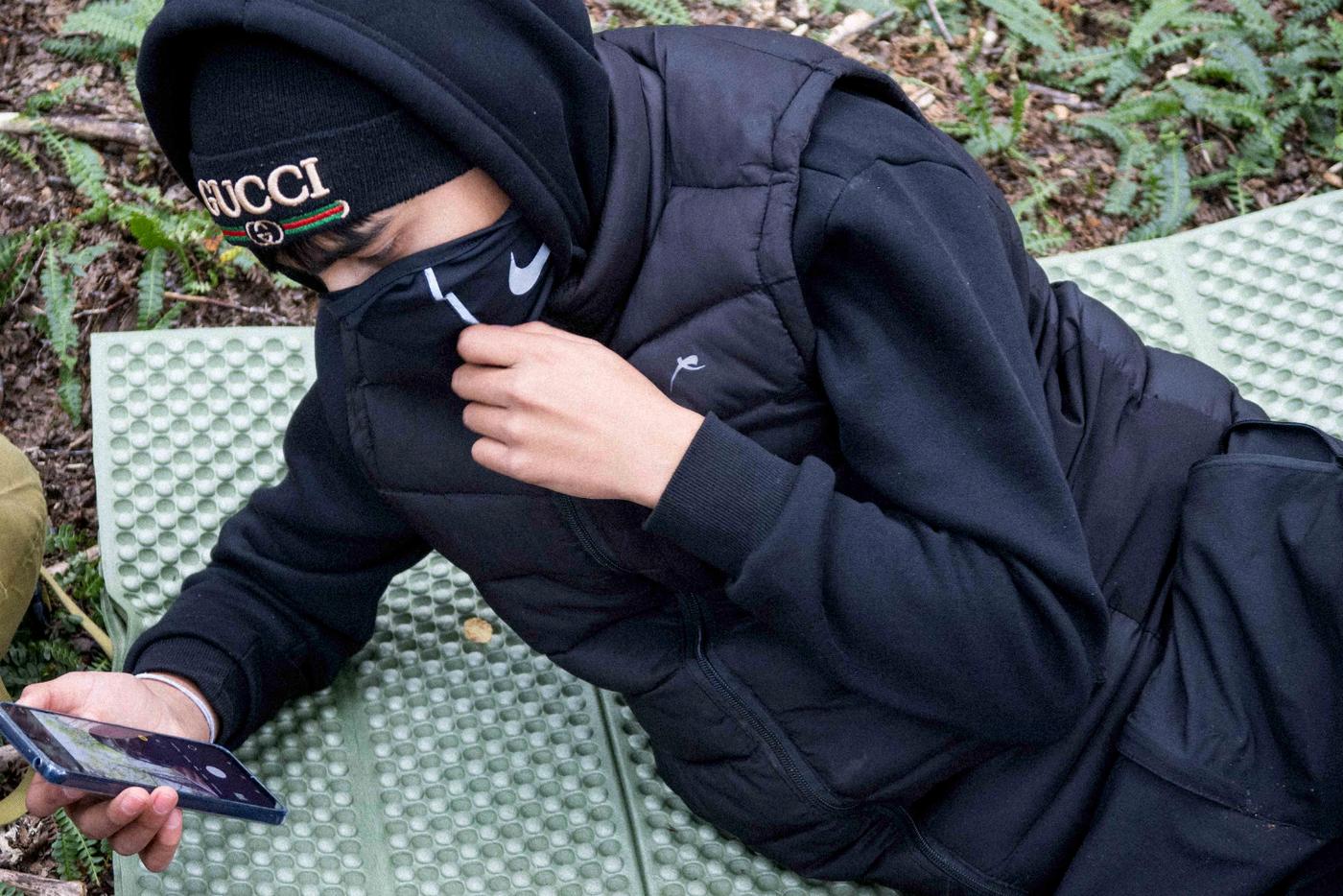 Un joven recostado sobre una colchoneta en el bosque mira la pantalla de su celular