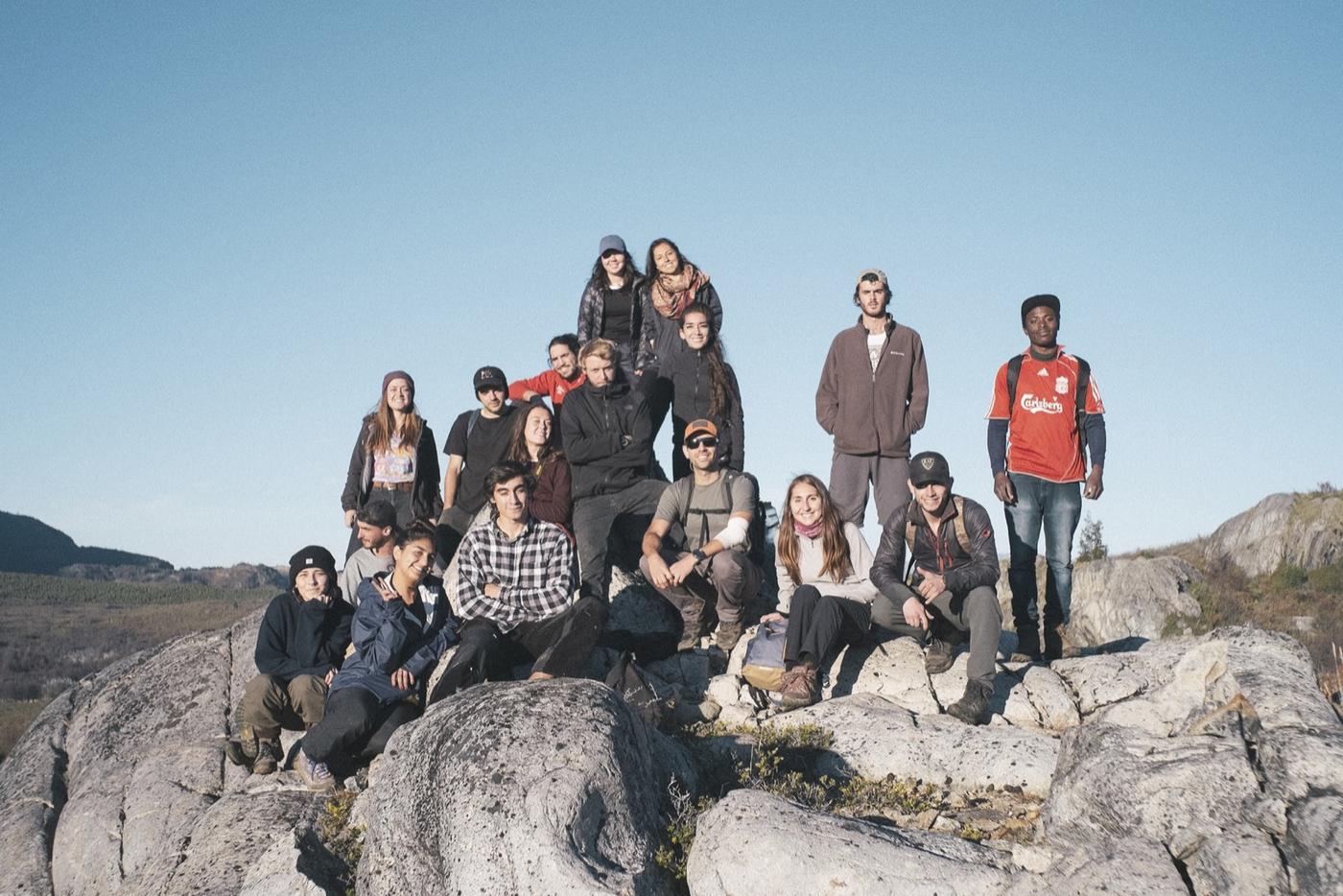 Un grupo de jóvenes y educadores posa sobre un roquerío en Aysén, con el valle y los cerros al fondo