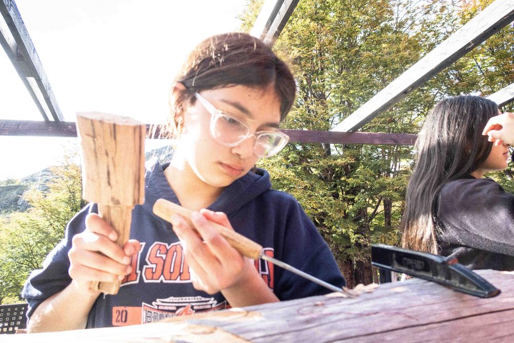 Una estudiante labra un trozo de madera junto a sus compañeras en el taller al aire libre