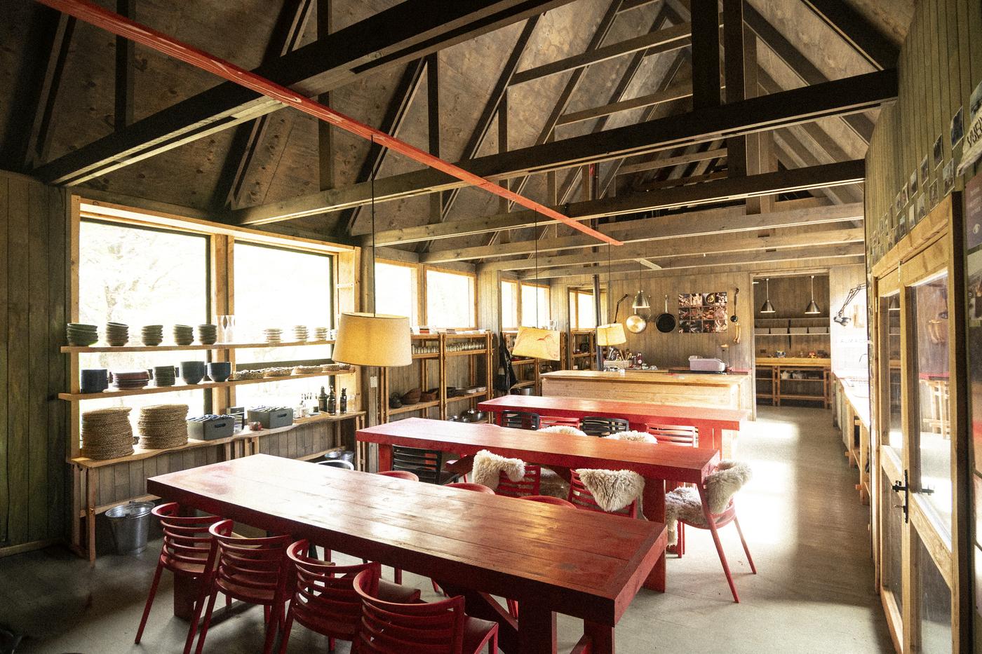 Comedor del Refugio Escuela con su mesa larga de madera, sillas rojas y lámparas colgantes