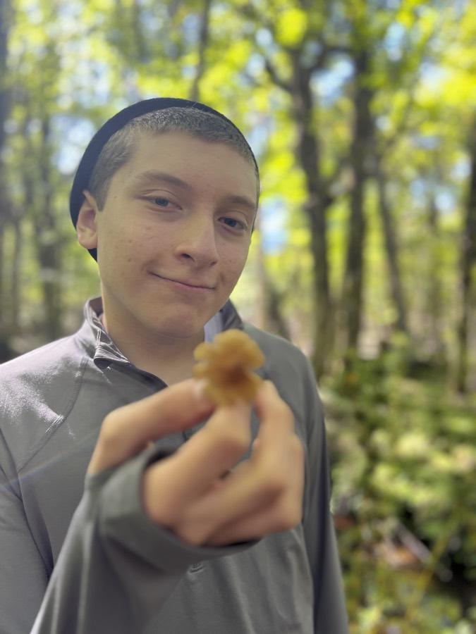 Un estudiante sonríe en el bosque mostrando un hongo en la mano