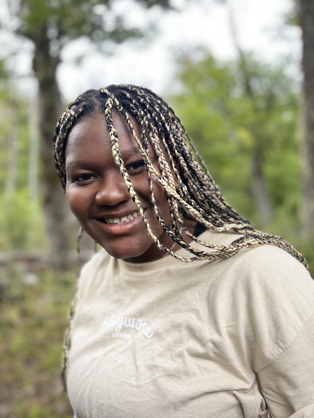 Una estudiante con trenzas sonríe en el bosque