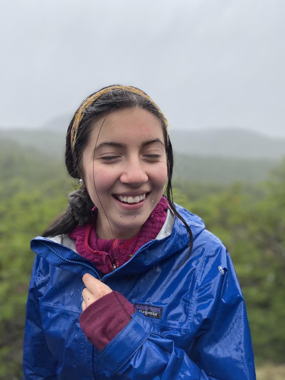 Una estudiante sonríe bajo la lluvia con una chaqueta azul