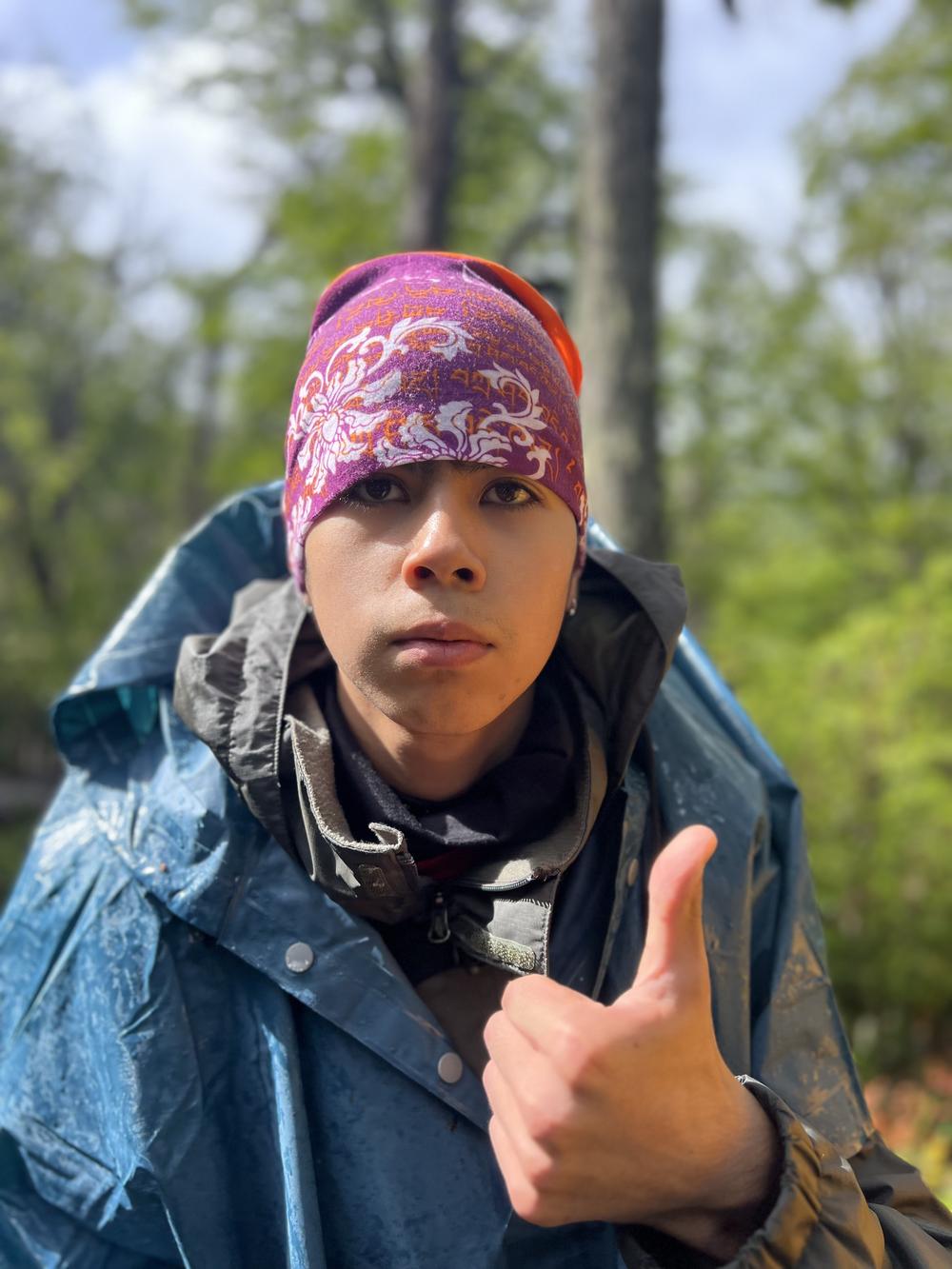 Un estudiante con pañuelo en la cabeza levanta el pulgar en el bosque